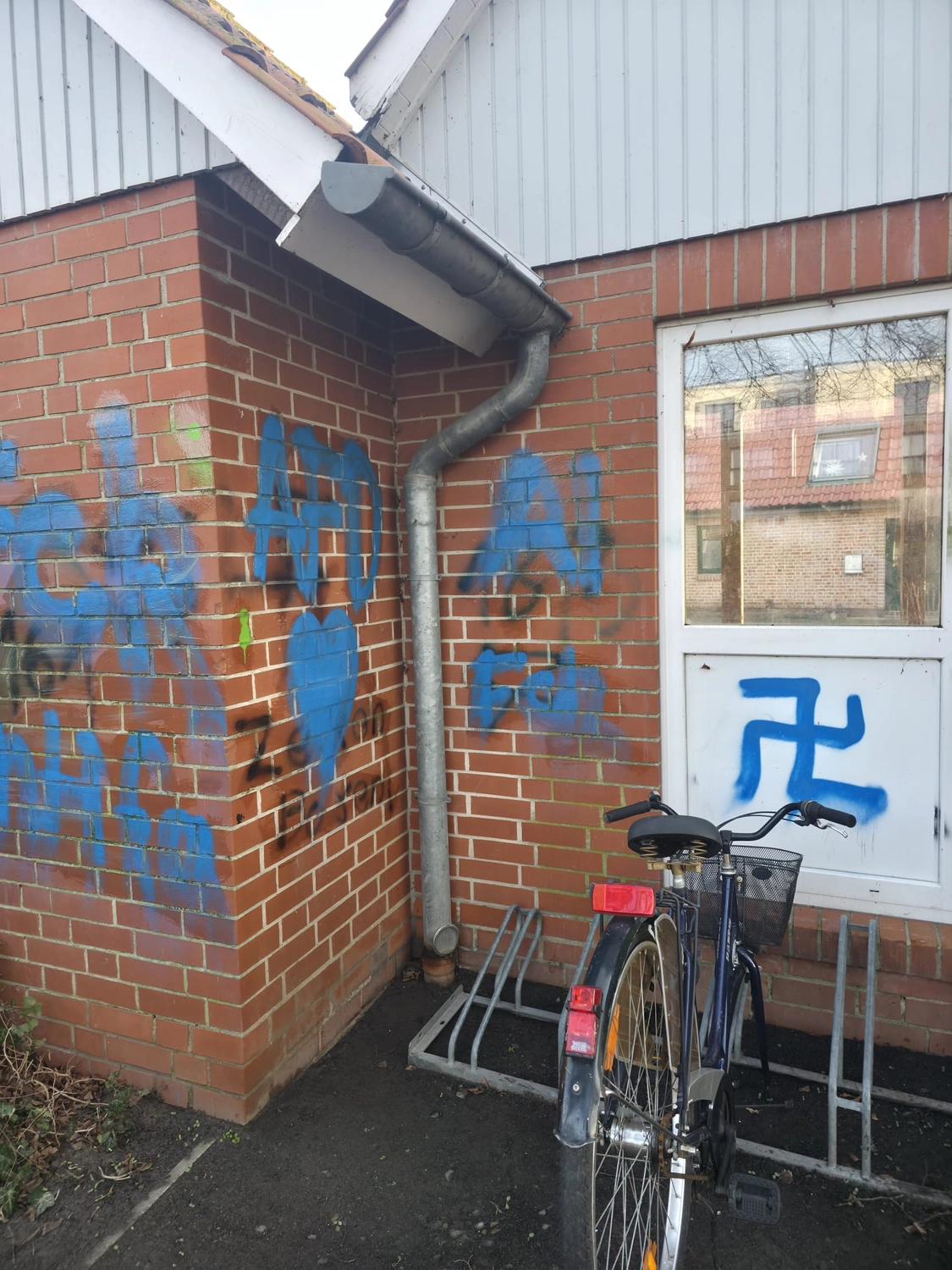 Duka Reinigung - Gebäudereinigung - Blaue Graffiti und ein Hakenkreuz an einer Backsteinmauer.