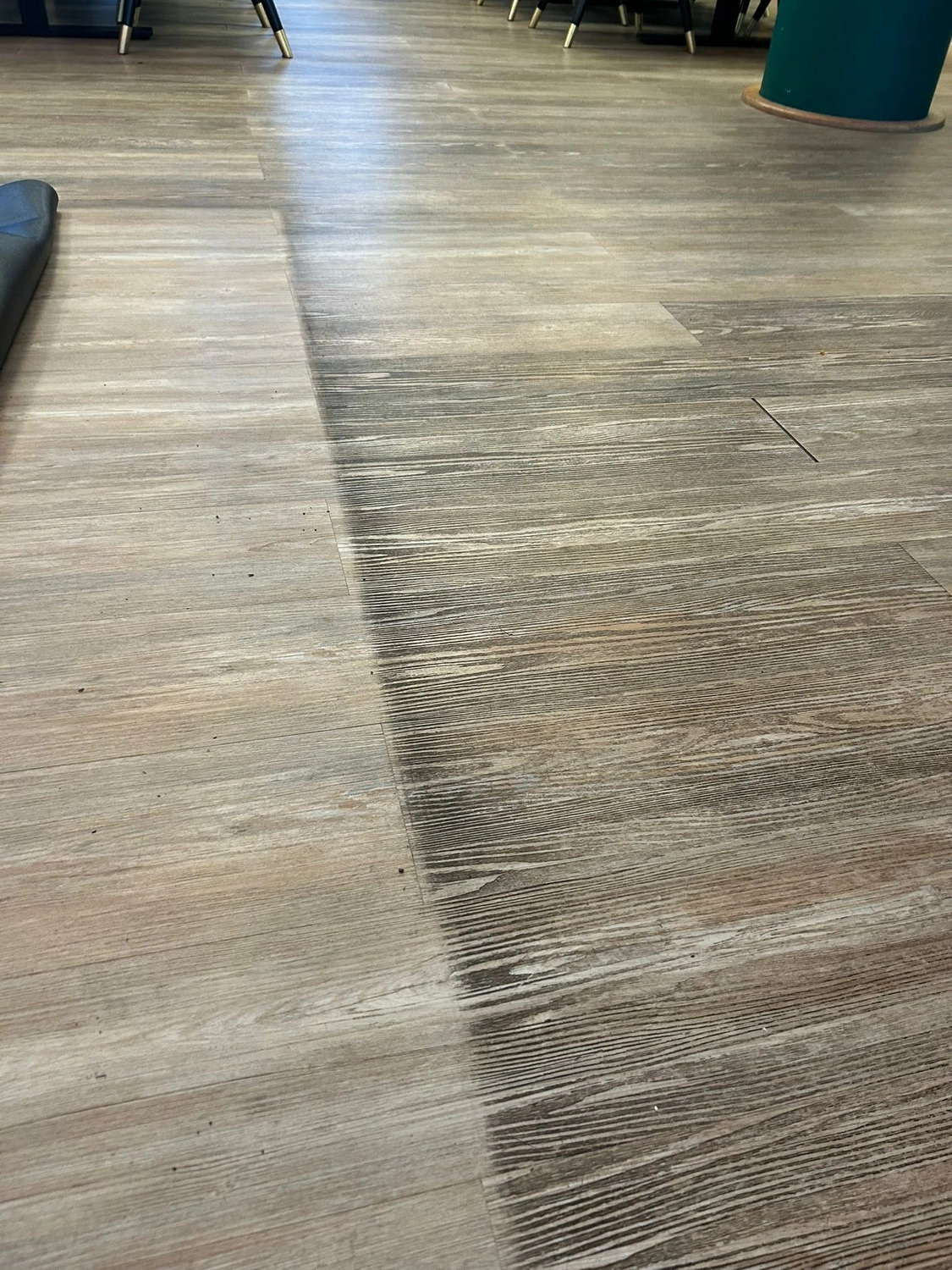 Duka Reinigung - Gebäudereinigung - Teilweise gereinigte Holzterrasse oder Vinylboden. Der starke Kontrast zwischen den hellen, restaurierten Dielen und der dunklen, ungewaschenen Oberfläche ist deutlich erkennbar.