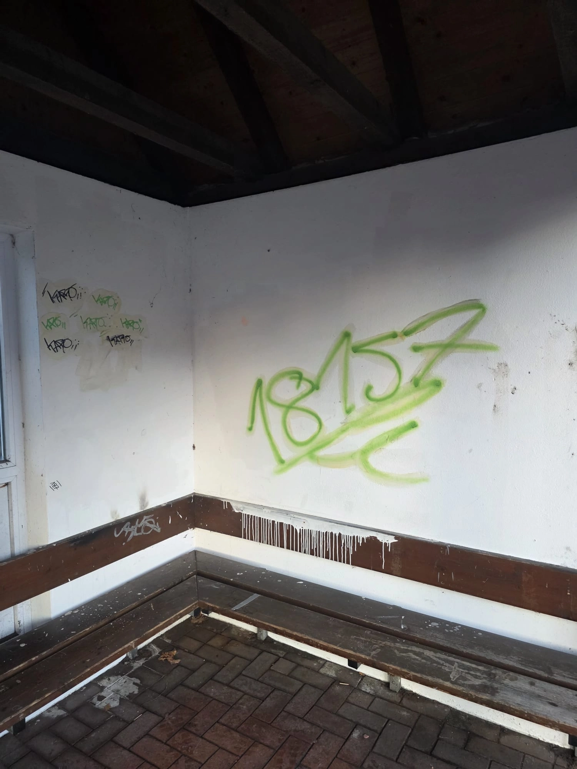 Duka Reinigung - Gebäudereinigung - Grüne Graffiti-Tags an einer weißen Innenwand vor der Reinigung.
