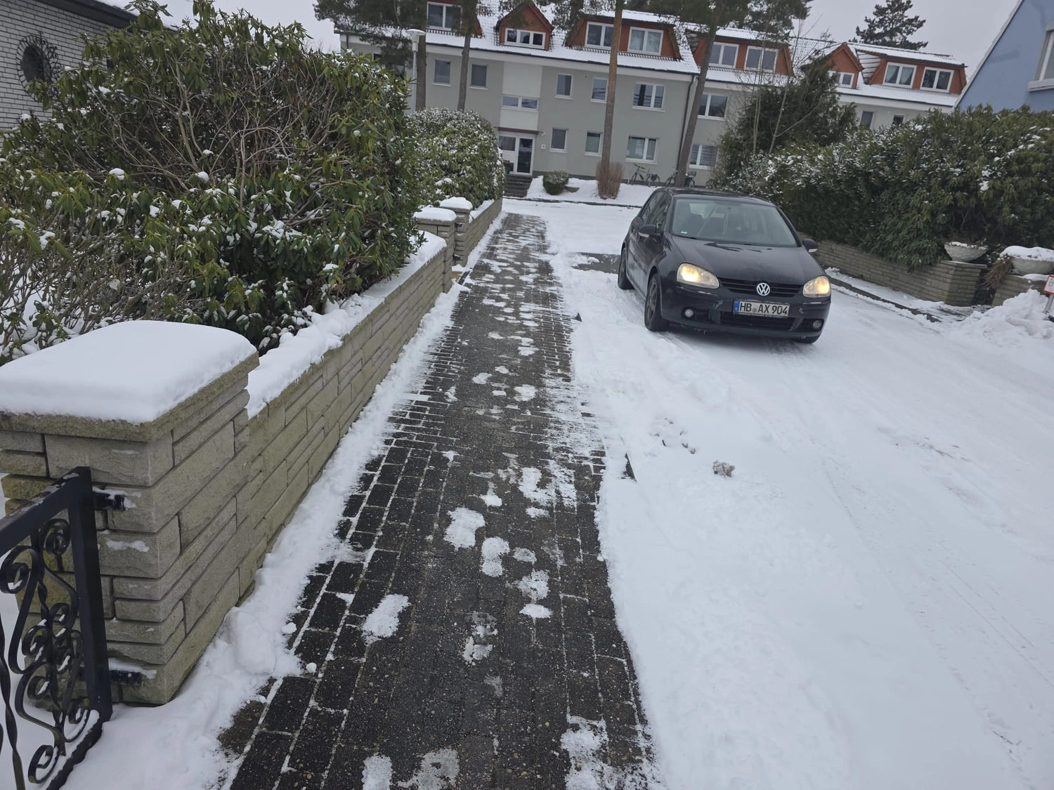 Duka Reinigung - Gebäudereinigung - Schwarzes Auto steht auf einem teilweise von Schnee und Schneematsch geräumten Backsteinweg.