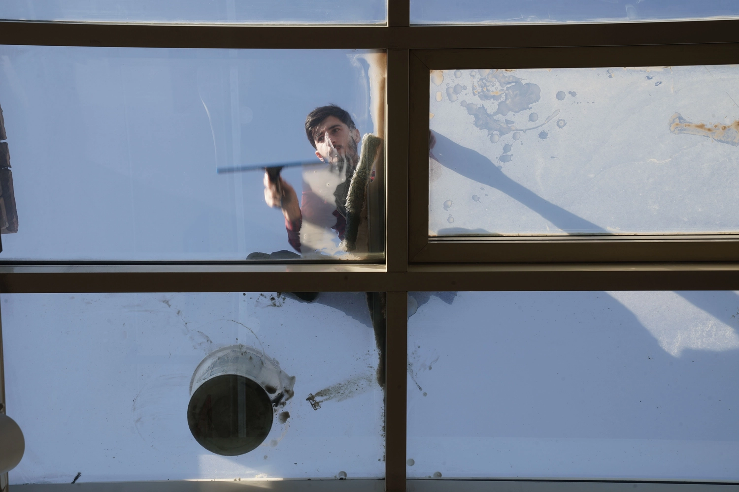 Duka Reinigung - Gebäudereinigung - Ein Reinigungskraft benutzt einen Abzieher auf dem Dach eines hohen Glaswintergartens.